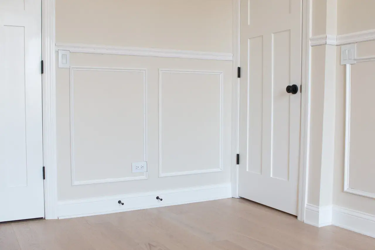 A room with a DIY chair rail, wainscoting, and white doors. The walls are painted a light cream color.
