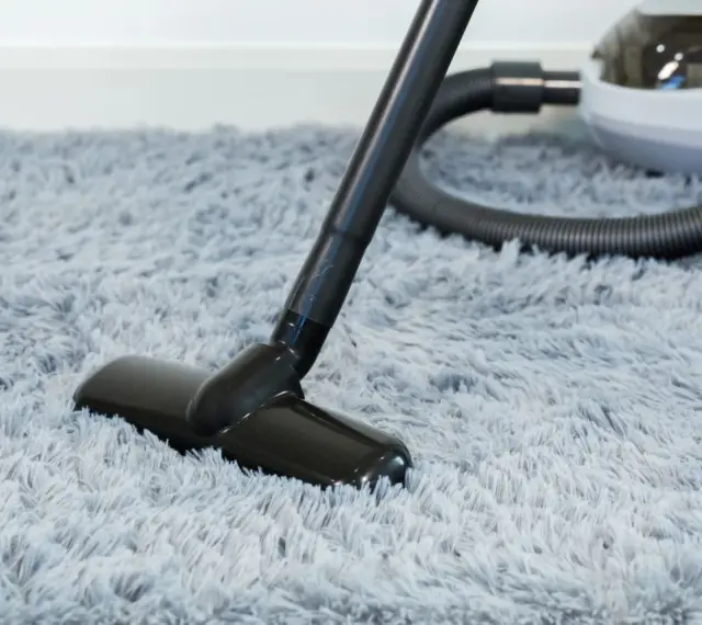 Vacuum cleaner head on a fluffy grey rug, demonstrating how to wash a rug by removing dust and debris.