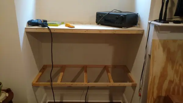 DIY project: a drill, screws, and audio receiver are on a shelf, with a wooden frame below, ready for how to hang shelves.