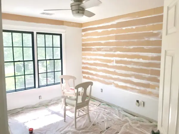 Room in progress, showing how to install shiplap on the wall. Two chairs sit on protective plastic sheeting.