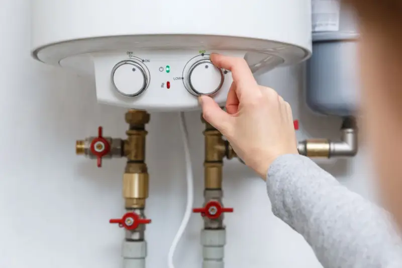 Adjusting the temperature dial on a water heater, showing its plumbing connections.