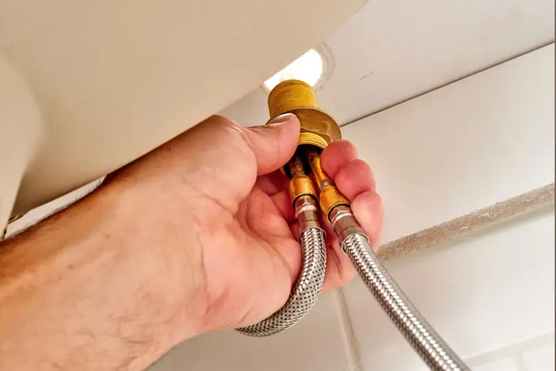Hands disconnect braided water supply lines from a faucet base, a key step in how to remove kitchen faucet.